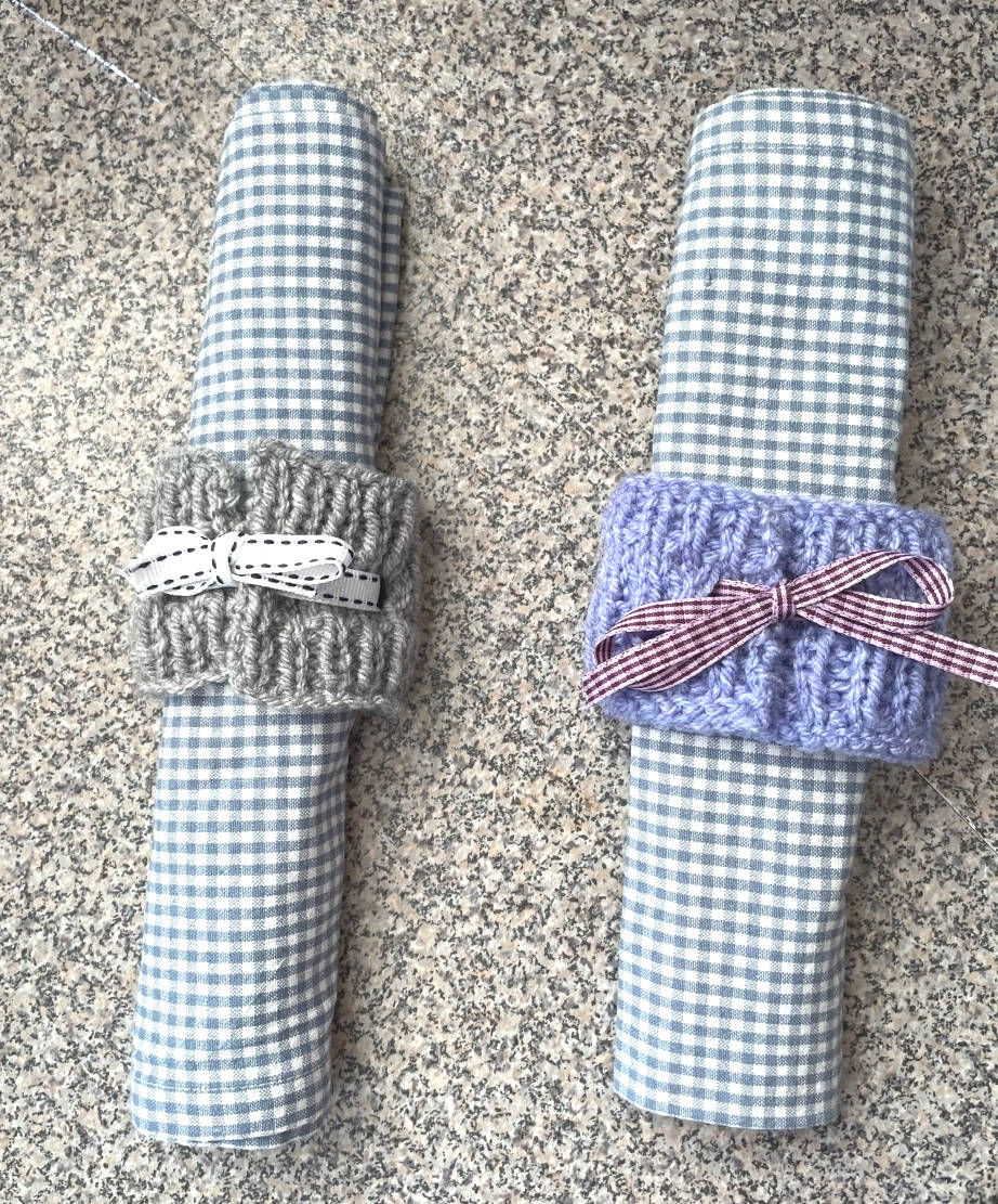 Two napkins with knitted napkin rings and bows on them.
