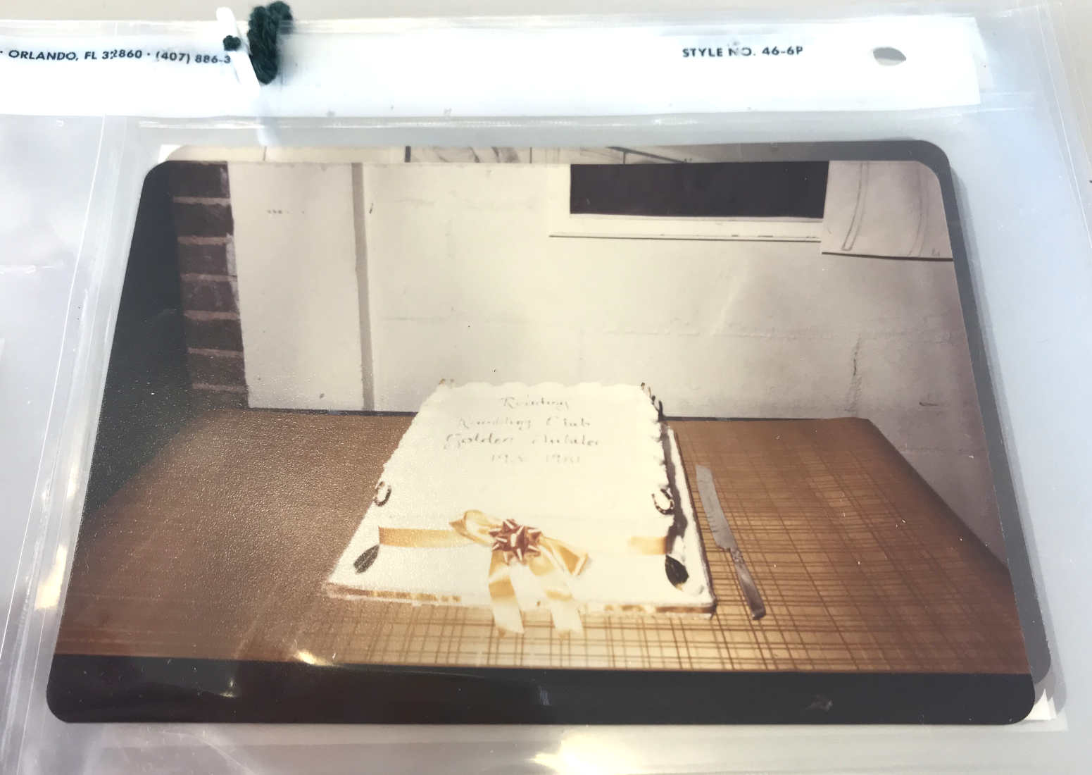 A photograph in its new archival packaging. Image shows a cake on a table. ref. D/EX2710/3/2